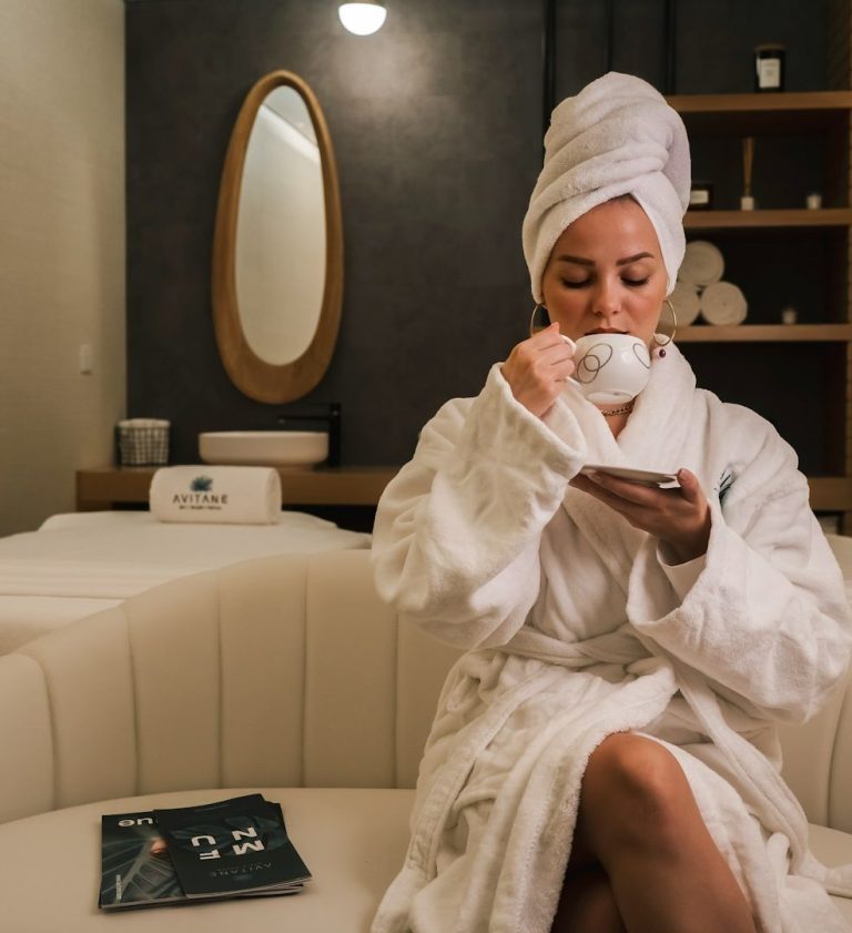 Frau mit Brille und Bluse sitzt an einem Tisch vor einer moosartigen Wand.