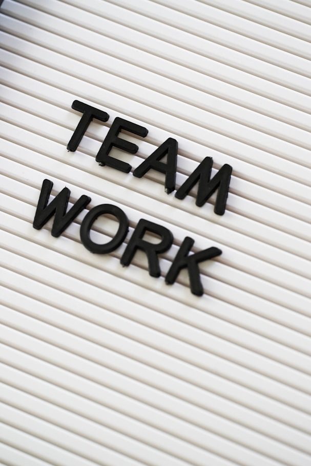 Frau mit Brille und Bluse sitzt an einem Tisch vor einer moosartigen Wand.