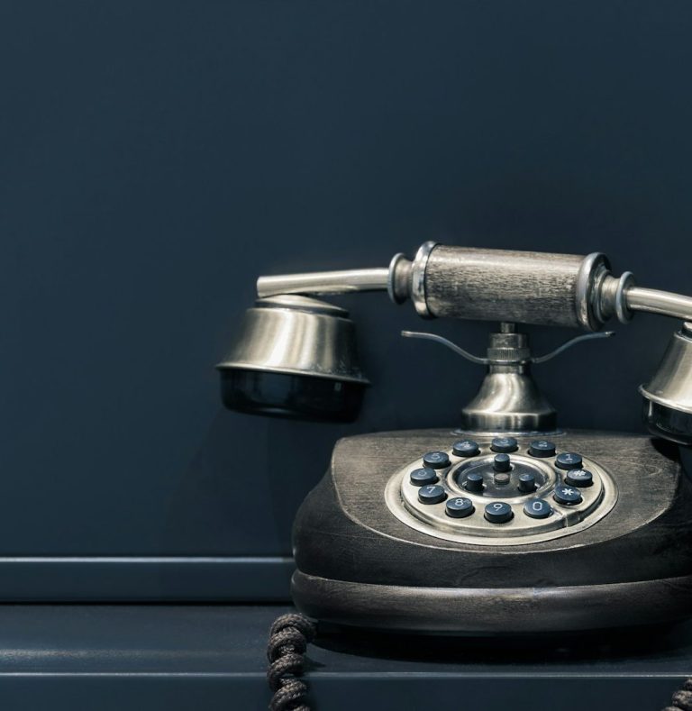 Frau mit Brille und Bluse sitzt an einem Tisch vor einer moosartigen Wand.