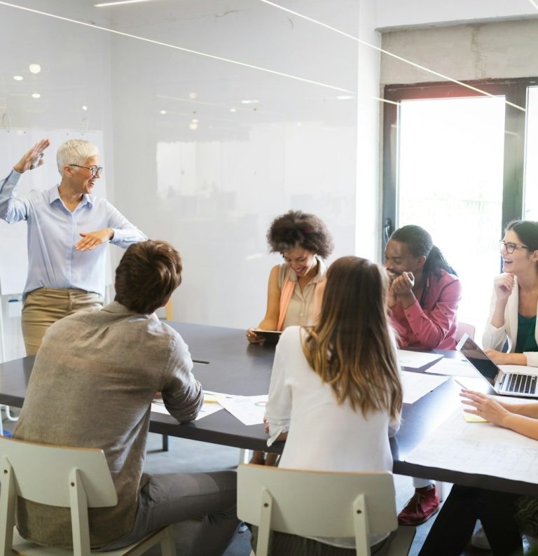 Frau mit Brille und Bluse sitzt an einem Tisch vor einer moosartigen Wand.