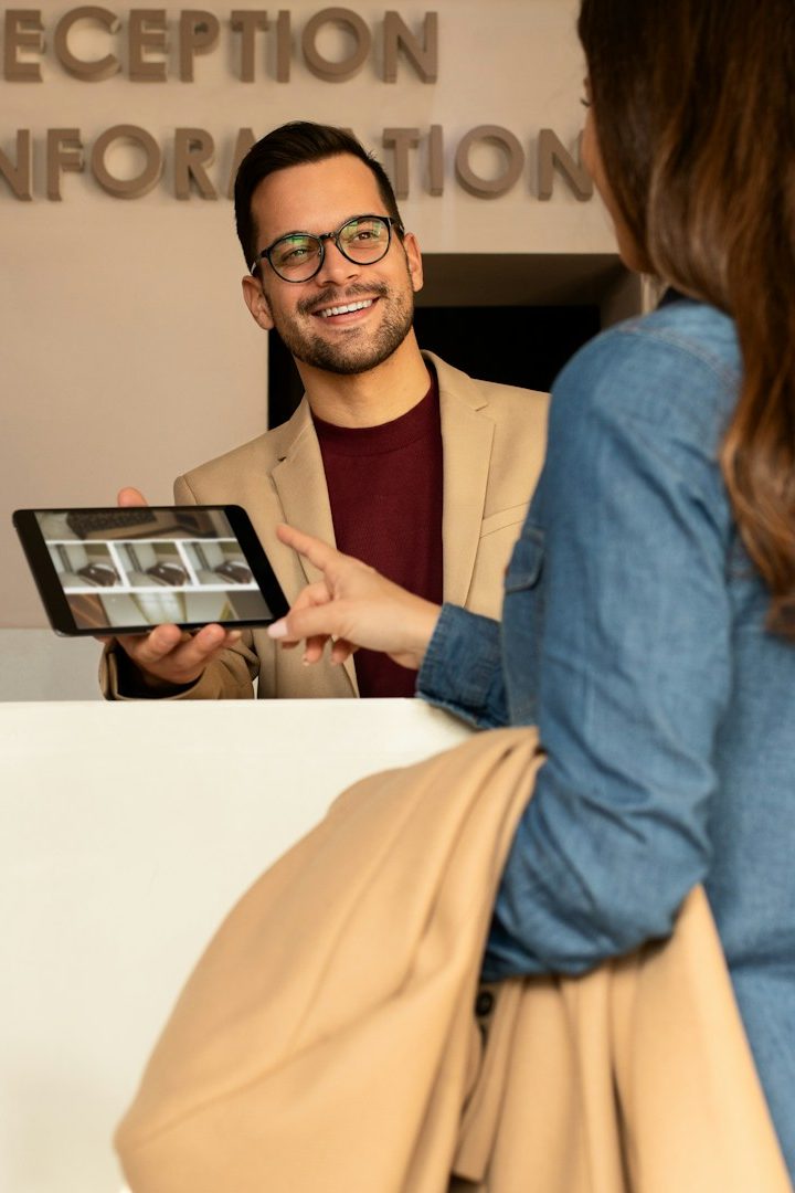 Frau mit Brille und Bluse sitzt an einem Tisch vor einer moosartigen Wand.